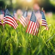 close up of American flags in green grass - ADL Auto Repair & Driveshafts Memorial Day Road Trip Prep
